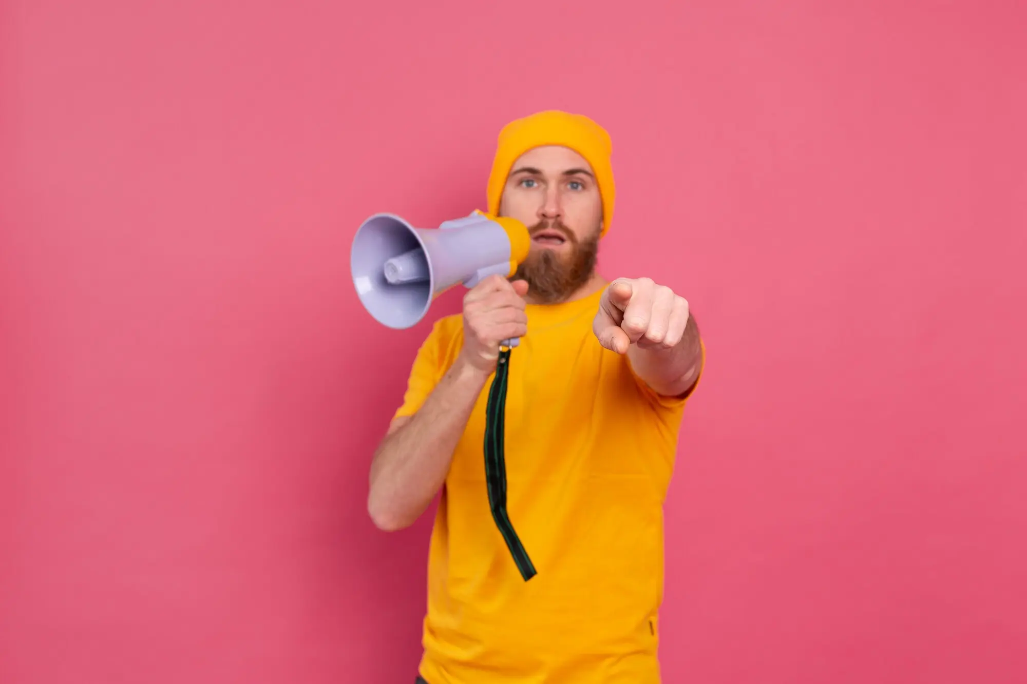 Achtung! Ein europäischer Mann mit Megafon zeigt mit dem Finger auf die Kamera, vor pinkem Hintergrund.